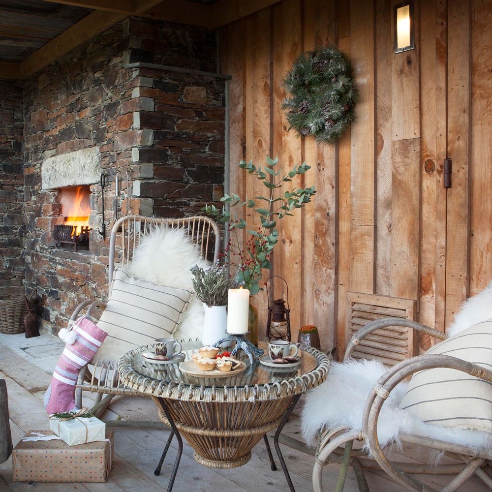 Terrasse décorée en hiver avec deux grands fauteuils, un feu extérieur et un goûter sur une table basse