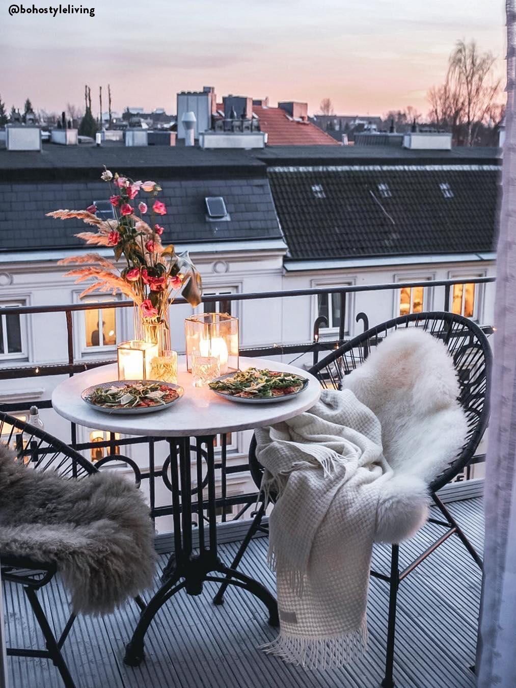 Balcon avec deux fauteuils et une table, avec un dîner romantique aux chandelles, des fleurs et des plaids : une inspiration pour décorer son balcon en hiver